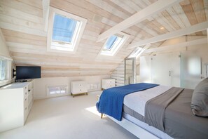 A bedroom with a sloped ceiling, skylights, a bed, a dresser, and a television. - Central, modern cottage with parking and water view (Provincetown)