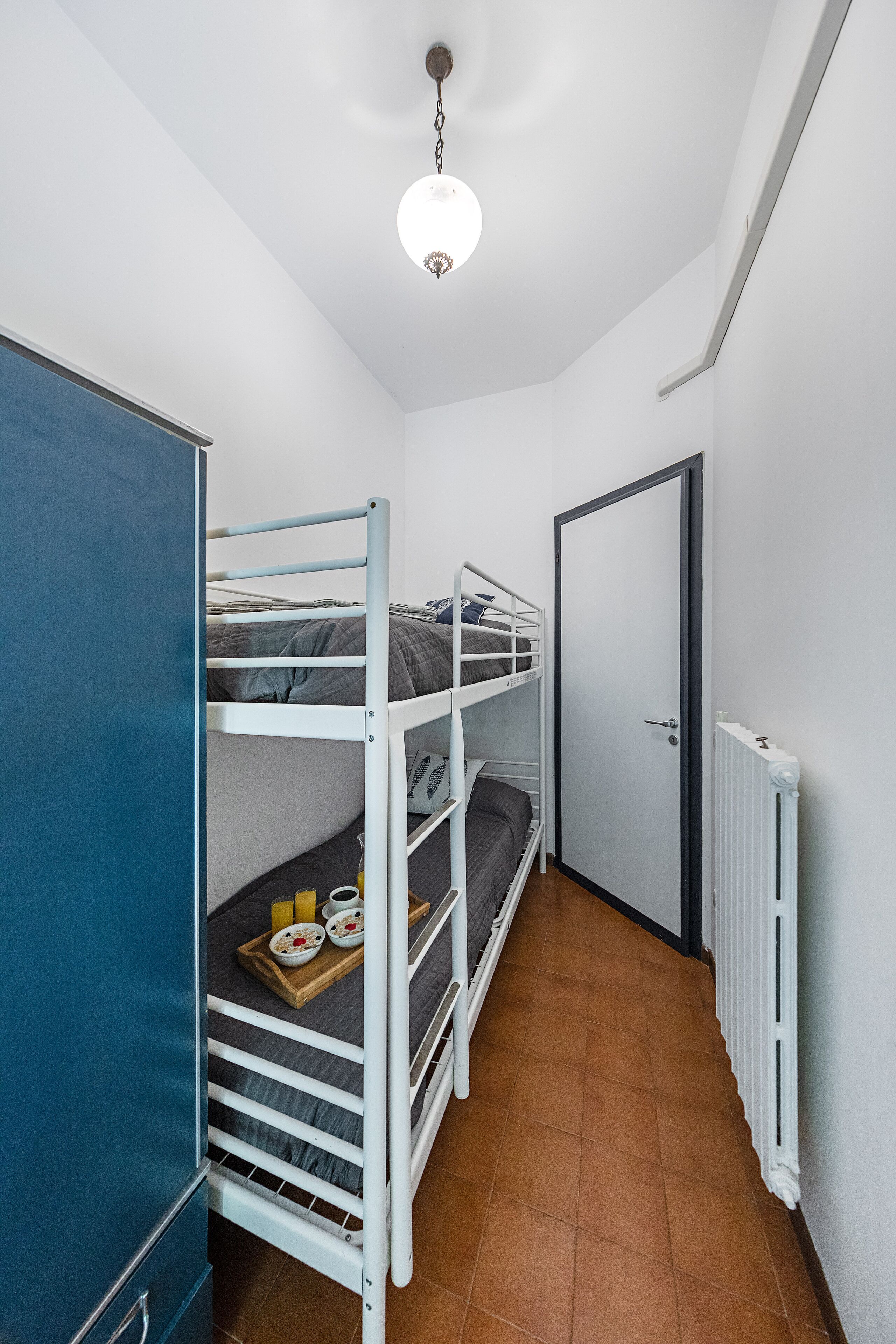 A dormitory room with bunk beds, a radiator, and a door.