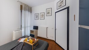Habitación de hotel ordenada con una cama, una mesita con desayuno, un escritorio y un radiador.