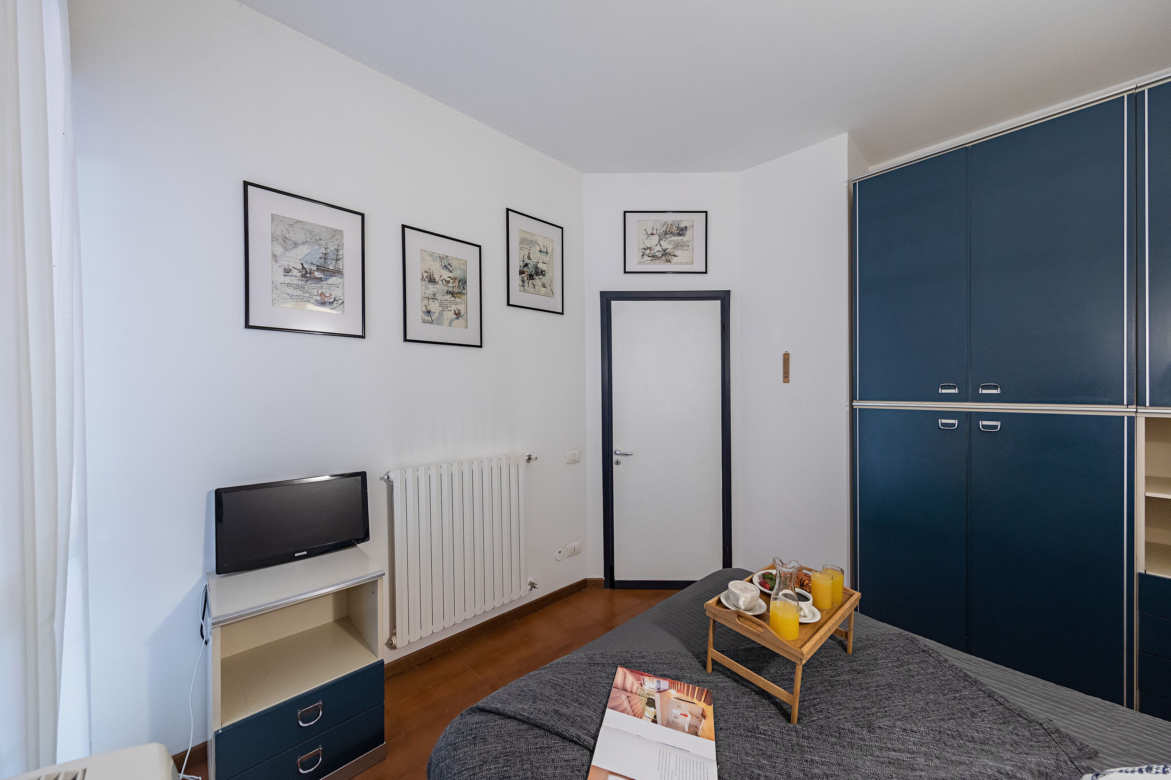 Une chambre à coucher avec un lit, une télévision, une armoire et des tableaux encadrés accrochés au mur.