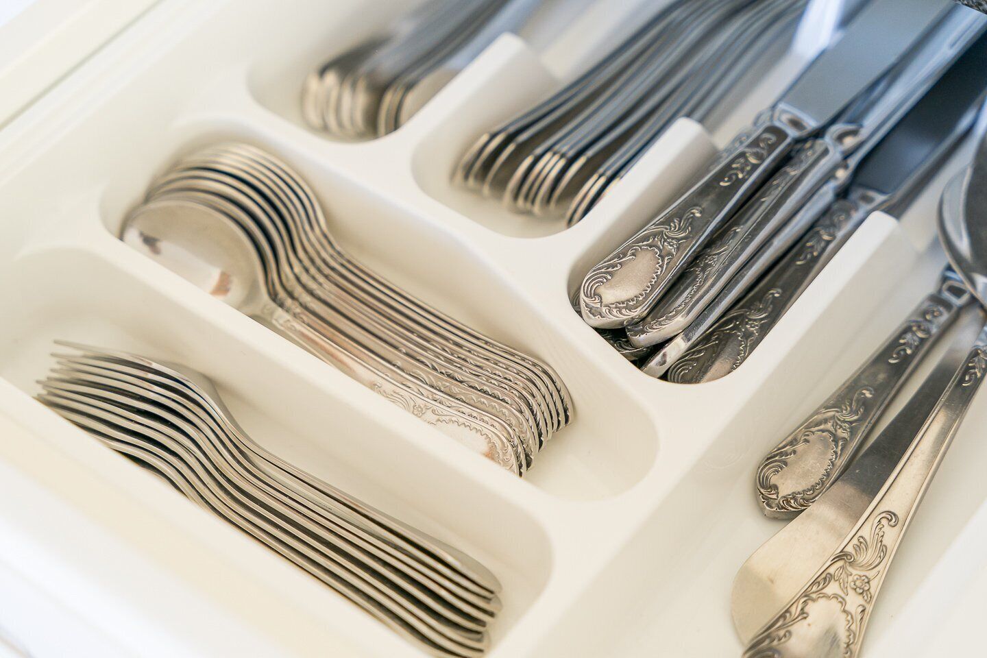 A set of silverware neatly arranged in a white box, including forks, knives, and spoons.