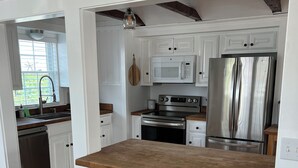 A modern kitchen with white cabinetry, stainless steel appliances, and a wooden countertop. - Plum Island Beach Cottage - 4 Minute Walk To Beach!! (Newbury)
