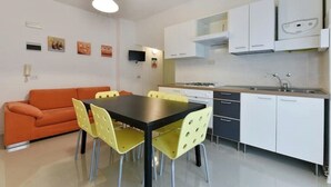 A compact kitchen with white cabinets, a black countertop, and a sink. There is a dining area with a black table and yellow chairs. - Lido di Jesolo, Italy. Entire accommodation (Lido di Jesolo)