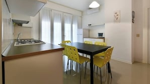 A compact kitchen with a gas stove, a dining table with yellow chairs, and a small refrigerator. - Lido di Jesolo, Italy. Entire accommodation (Lido di Jesolo)