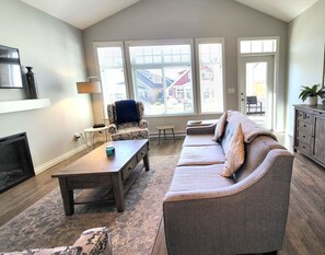 Una sala de estar con sofá, mesa de centro, chimenea y ventanas amplias.