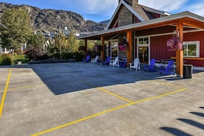 Un espacio al aire libre cubierto con sillas y mesas, un edificio de fachada roja y un telón de fondo montañoso.