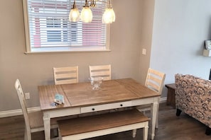 Un comedor con una mesa de madera, cuatro sillas, un banco y un sofá estampado.