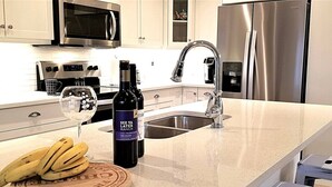 A kitchen with stainless steel appliances, a wine bottle, and bananas on a wooden board.