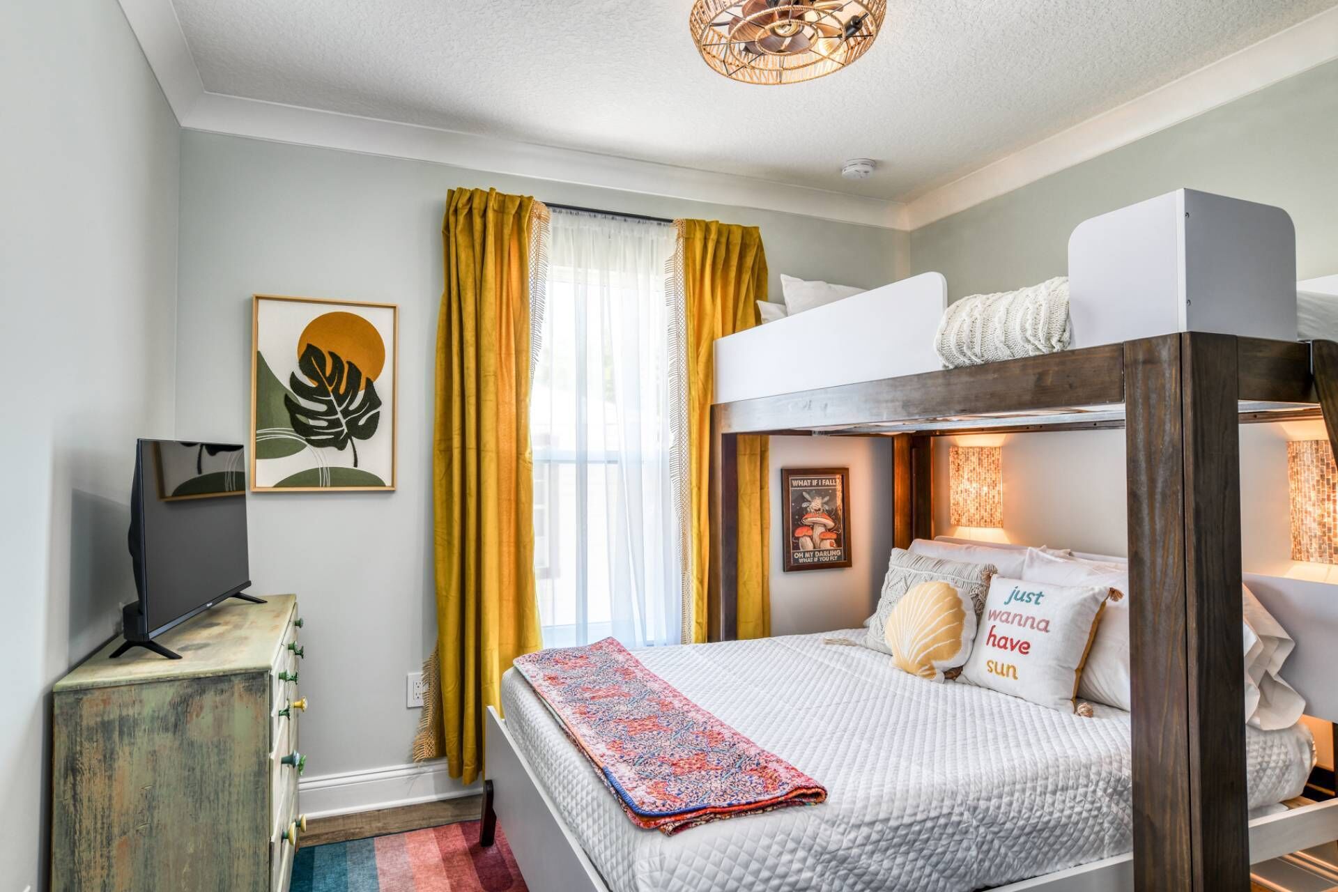 A bedroom with a bunk bed, a television on a cabinet, a framed artwork, and a poster on the wall.