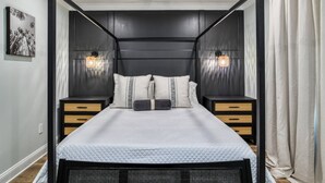 A modern bedroom with a black metal frame canopy bed, white bedding, two bedside tables with woven baskets, and wall-mounted lamps. - Lincolnville Nook (St. Augustine)