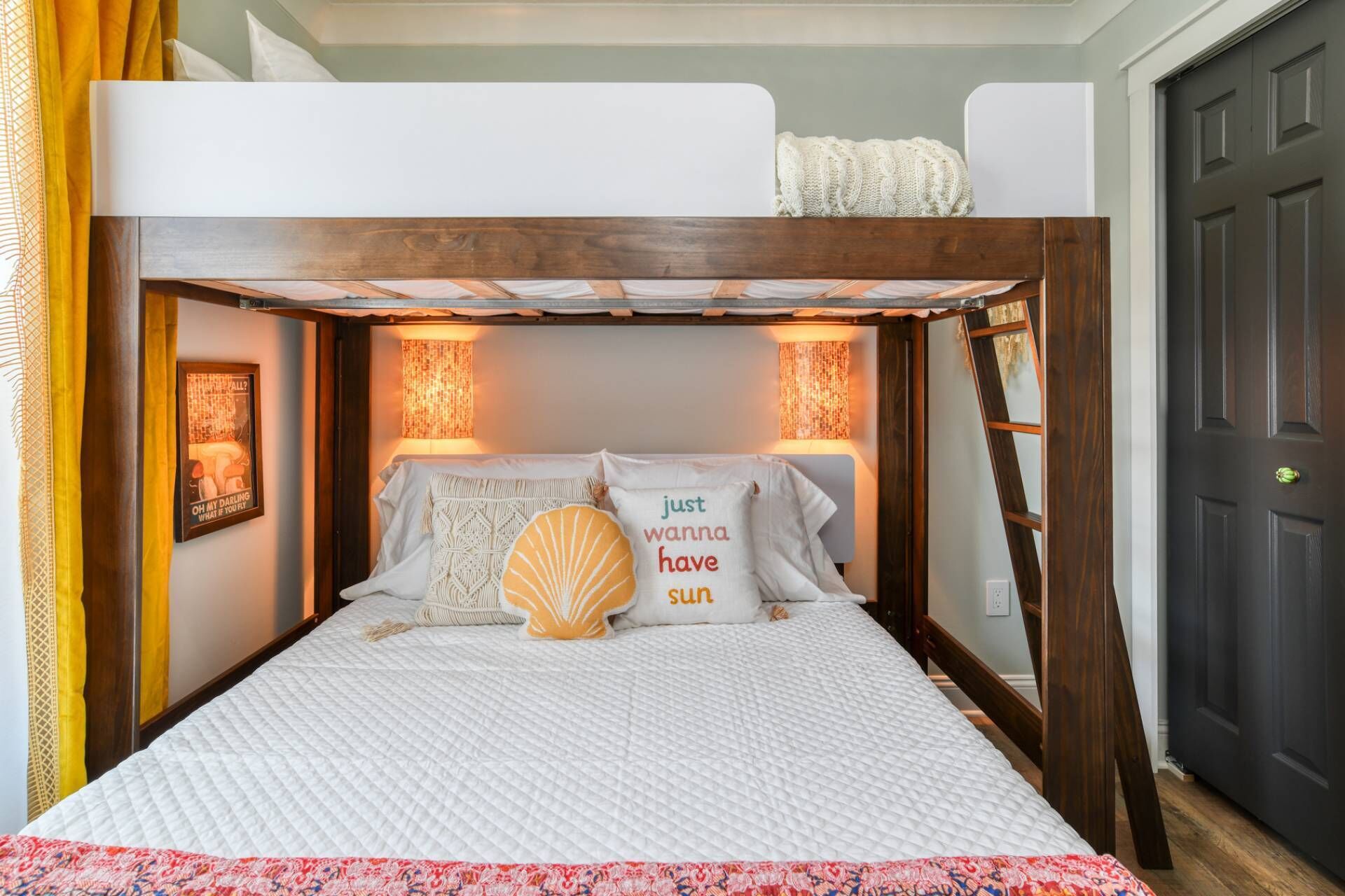 Un lit superposé avec un matelas matelassé blanc, un coussin décoratif en forme de coquillage et deux lampes fixées au mur.