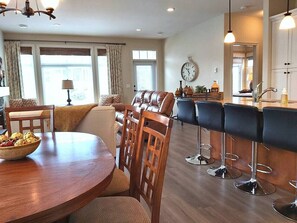 A dining area with a round wooden table, chairs, and a bar with stools.