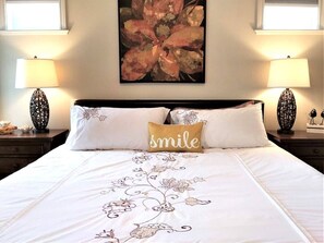 A neatly made bed with floral embroidery, a pillow with the word 'smile,' and two lamps on either side.
