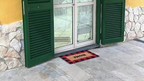 A house entrance with green shutters, a stone wall, and a doormat.