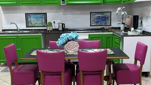 A kitchen with green cabinets, a dining table with six chairs, and a tiled floor.