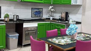 A compact kitchen with green cabinets, a dining table with pink chairs, and a tiled floor.