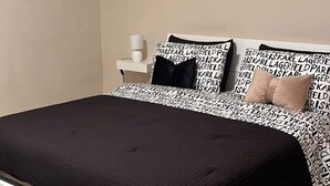 A bedroom with a white bed, black and white patterned headboard, and a single wall-mounted air conditioner.