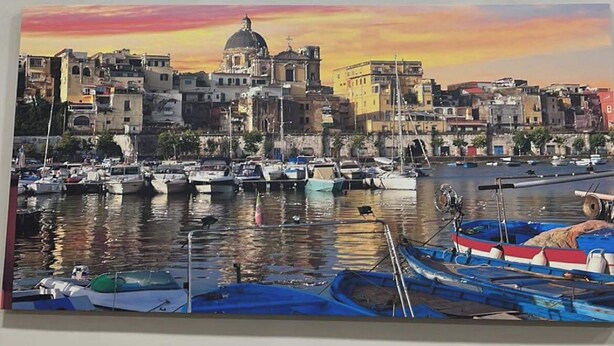 A painting of a harbor with boats and buildings, hung above a window.