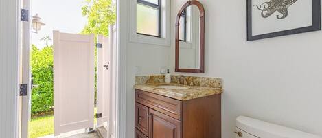 A bathroom with a wooden vanity, a sink, a toilet, a window, and a framed artwork on the wall.
