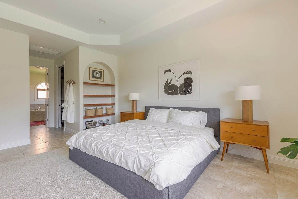 Une chambre à coucher avec un grand lit, deux tables de chevet, une armoire et une salle de bain visible à travers une porte ouverte.