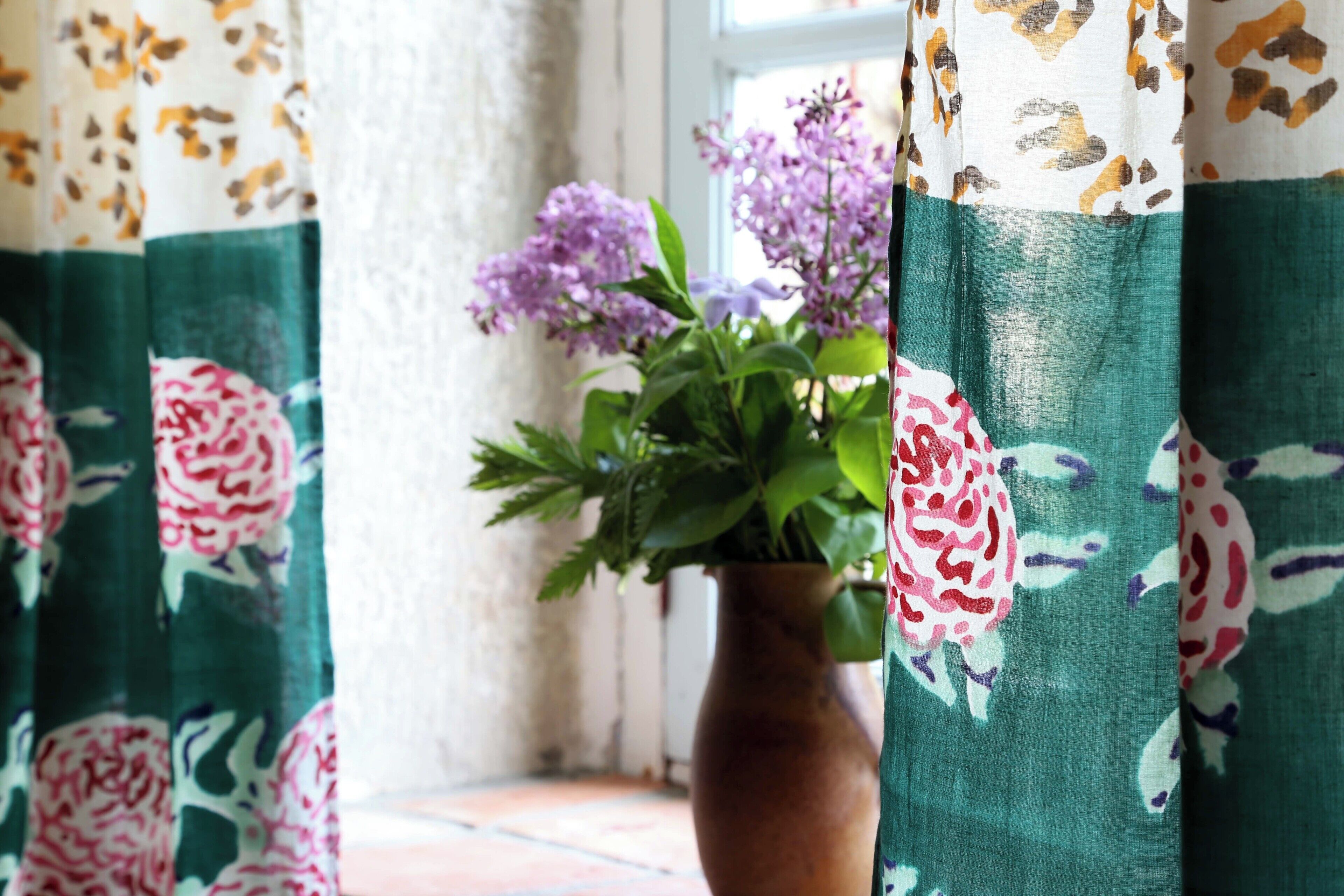 Ein Zimmer mit Fenster, Blumentopf und Vorhängen mit floralem Muster.