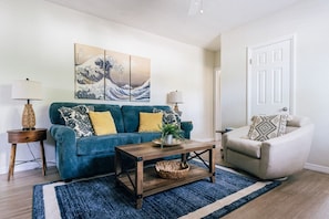 Un salon avec un canapé bleu, une table basse en bois et un fauteuil à motifs.