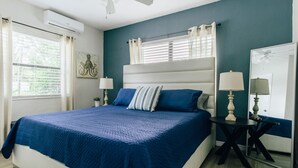 Un dormitorio con cama, dos mesitas de noche, ventilador de techo y una ventana con persianas.