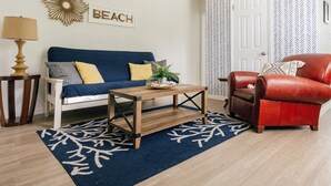 Un salón con un sofá azul, una mesa de centro de madera, un sillón de cuero rojo, una lámpara y una pared con un letrero que dice 'BEACH'.