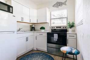 A kitchen with white cabinets, a stove, a microwave, a sink, and a window with blinds. - One bedroom private apt 2 blocks to beach (Pompano Beach)