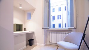 A modern, minimalistic room with a white chair, a small desk, and a radiator. - Cunabu Emilio (Rome)