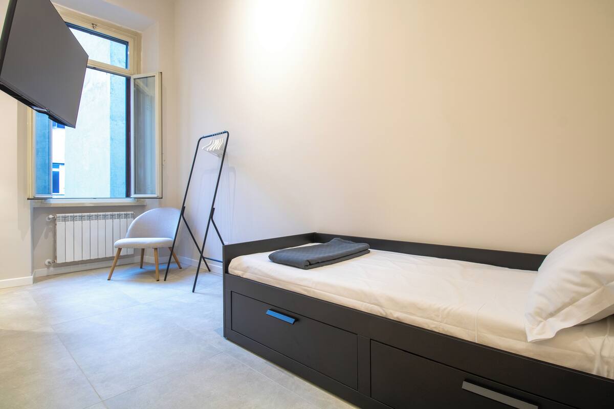 Un dormitorio con cama, una silla, un radiador y una ventana.