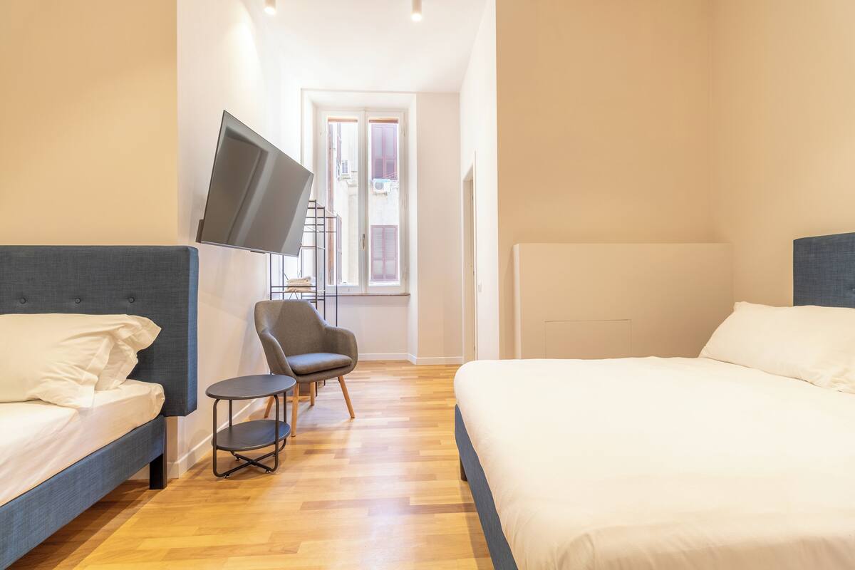 Un dormitorio con dos camas, un televisor en la pared, una silla y una ventana con persianas.