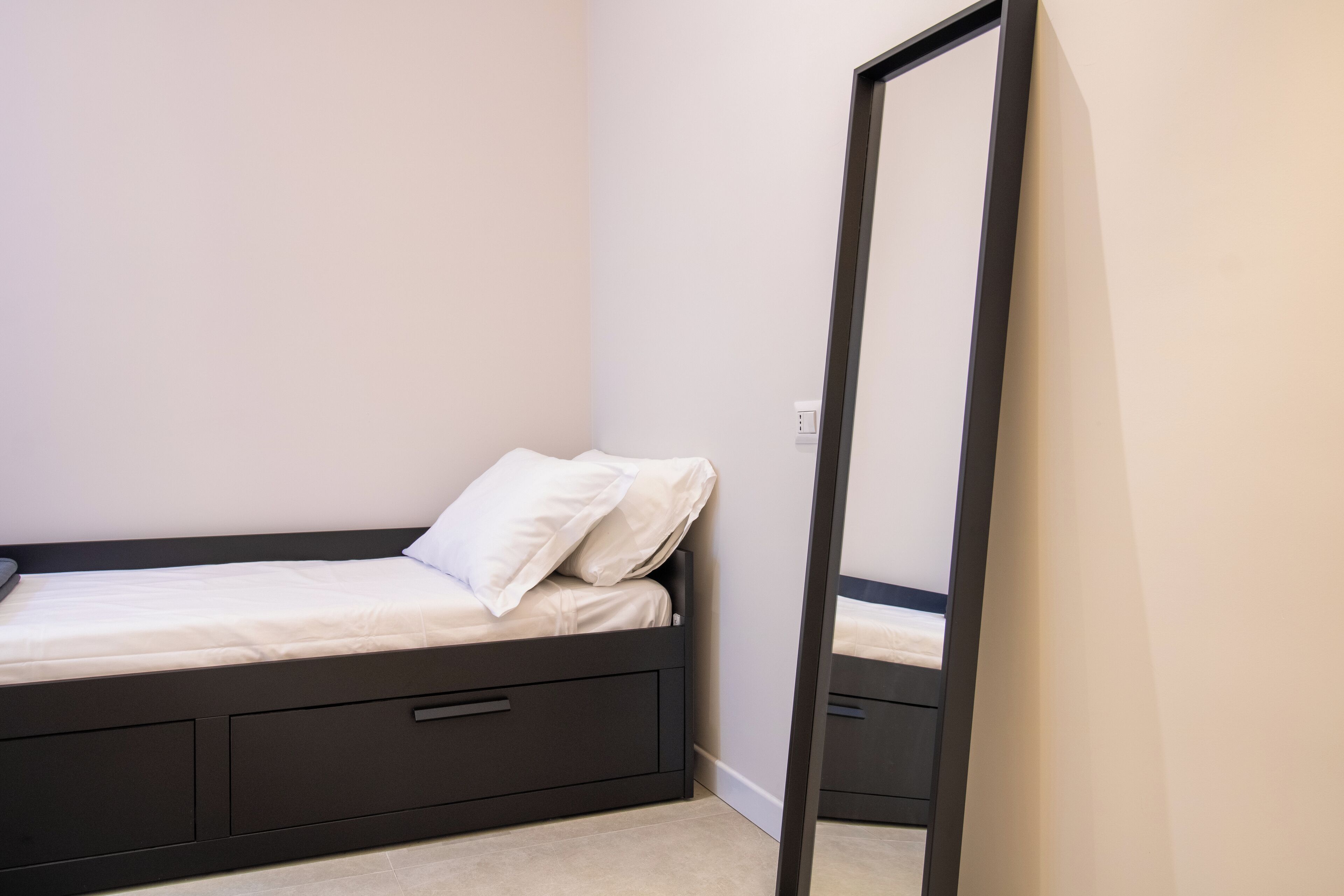 A small, neatly arranged bedroom with a single bed, a dresser, and a mirror.