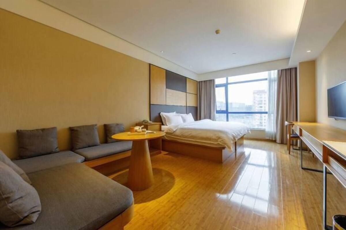 A modern hotel room with a large bed, a sofa, a small table, and a TV.