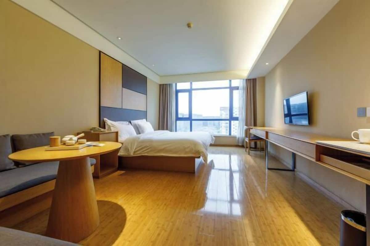 A modern hotel room with a bed, a desk, a sofa, a round table, and a TV.