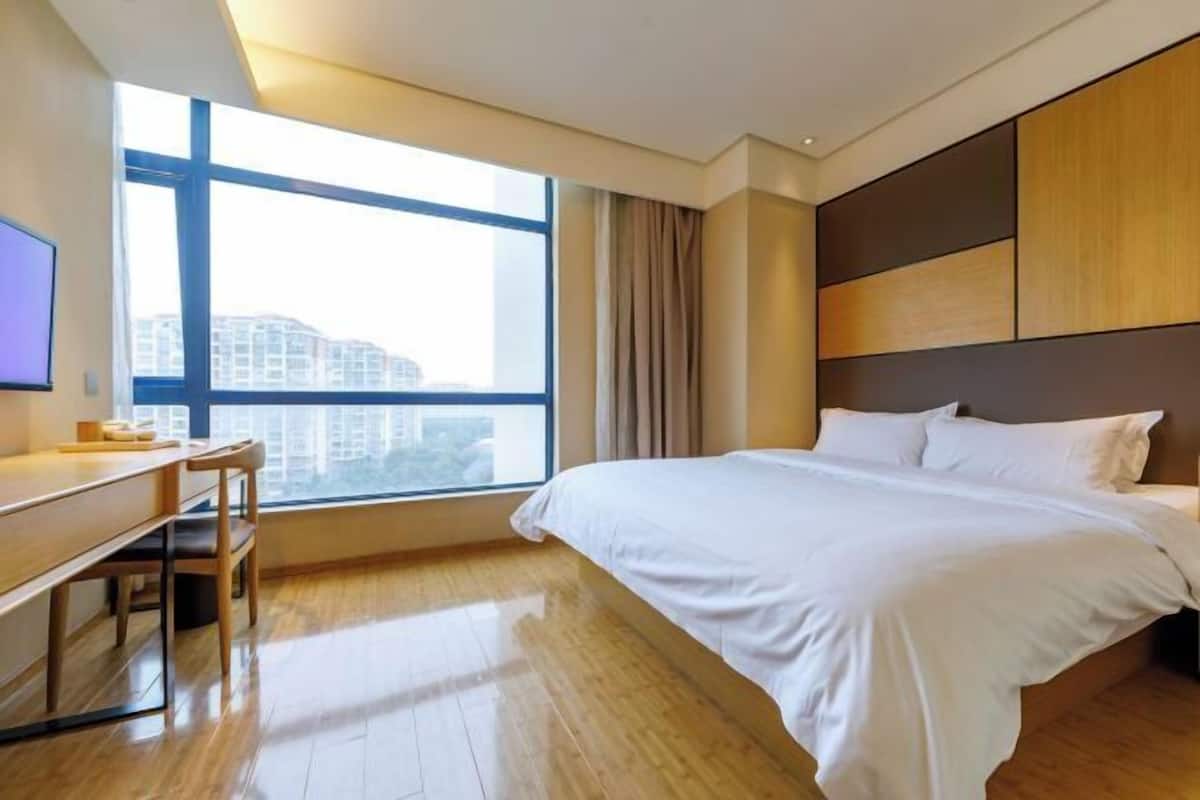 A hotel room with a large window, a bed, a desk, and a television.