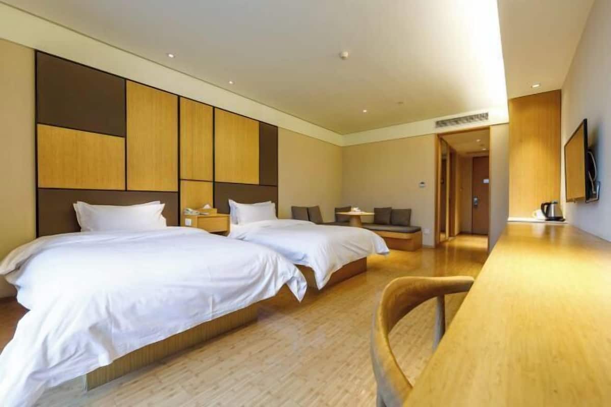 A hotel room with two beds, a wooden desk, and a TV on the wall.