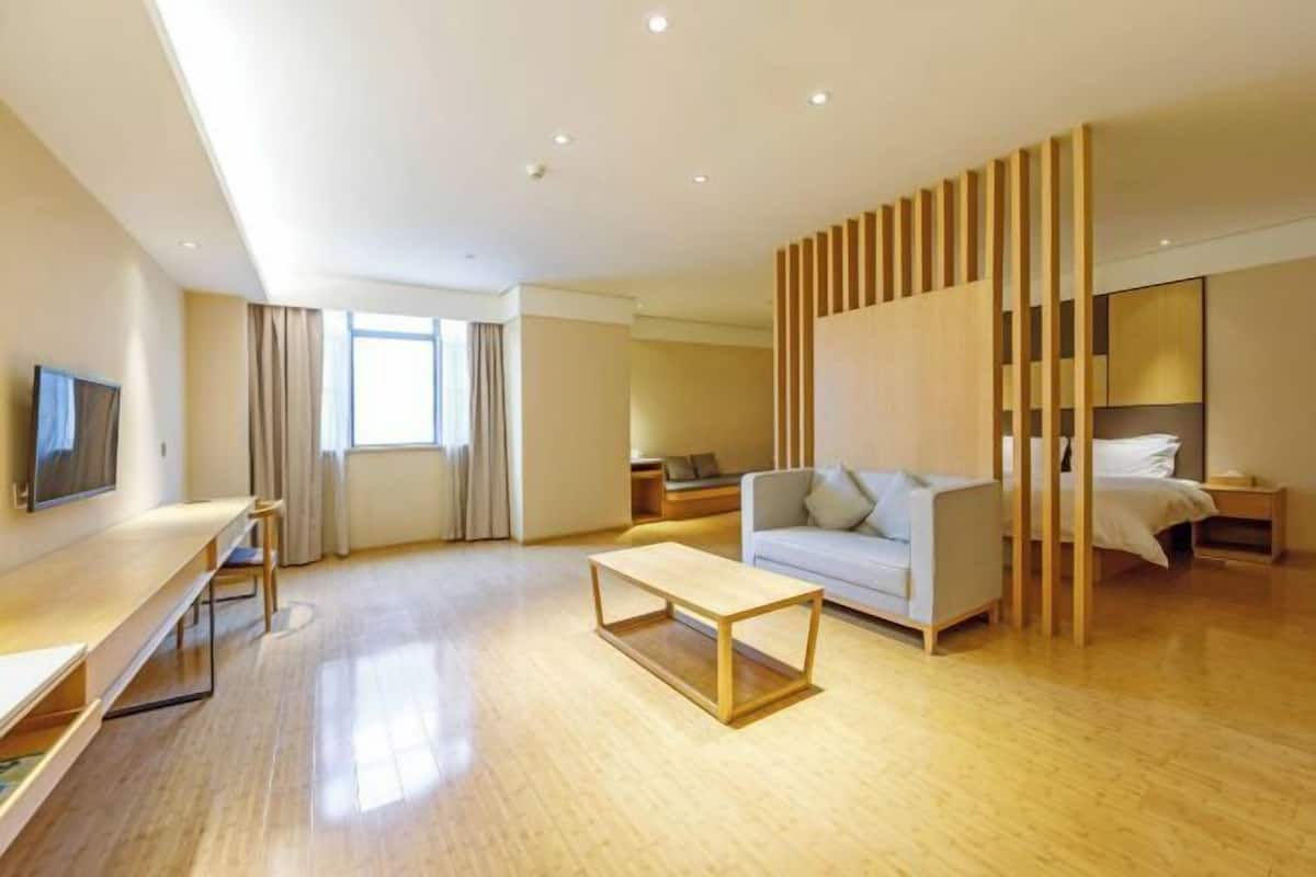 A modern hotel room with a wooden floor, a sofa, a TV, a desk, and a bed.