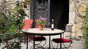 Un edificio de piedra con una mesa redonda y sillas, un jarrón con flores y una botella de vino.