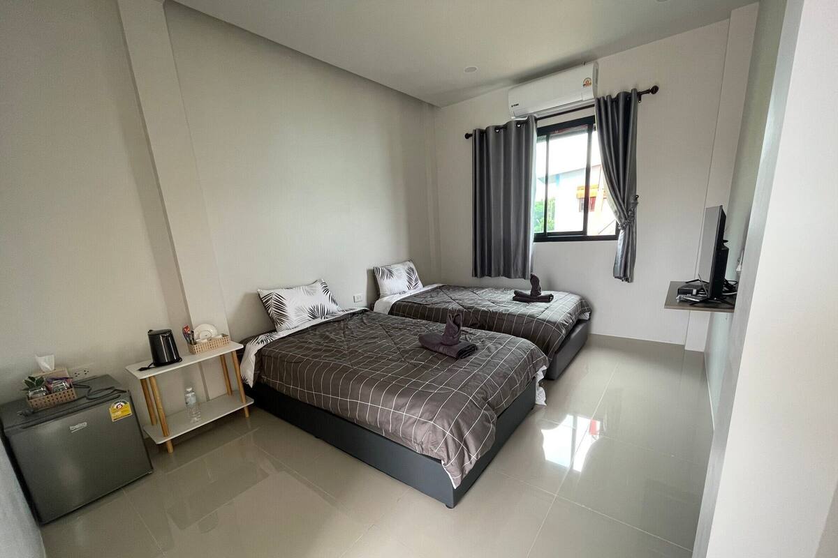 Habitación de hotel moderna con dos camas, un escritorio pequeño, un refrigerador y una ventana con cortinas.