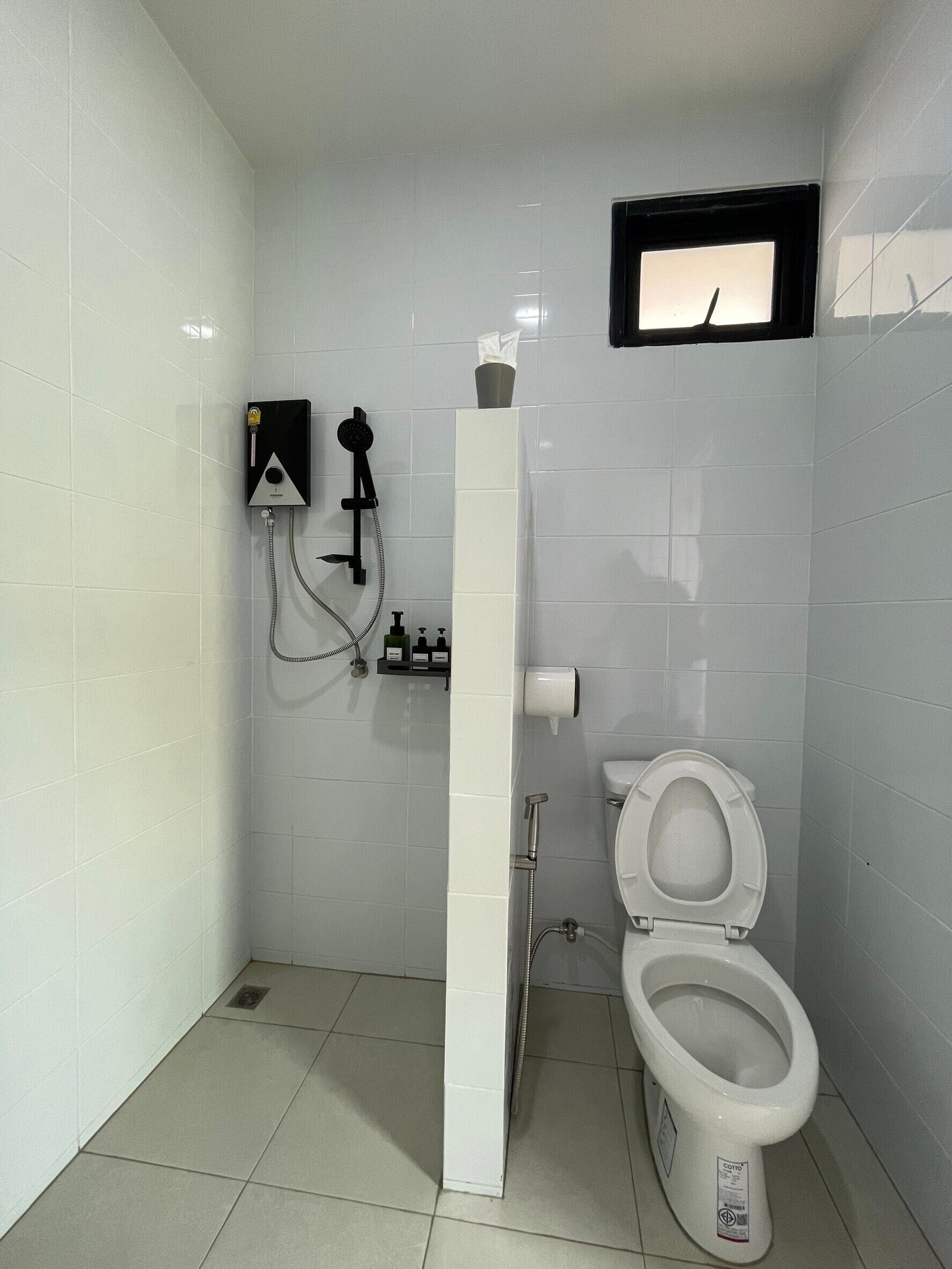 A small, white-tiled bathroom with a toilet, a shower unit, and a hand dryer.
