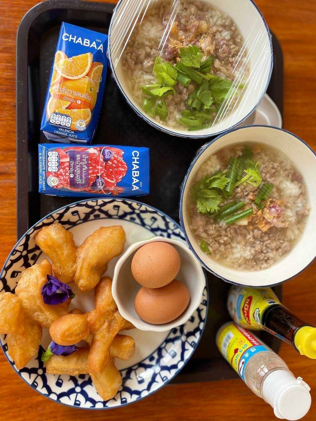 A tray with two bowls of soup, a plate of fried snacks, a cup of orange juice, and a bottle of sauce.
