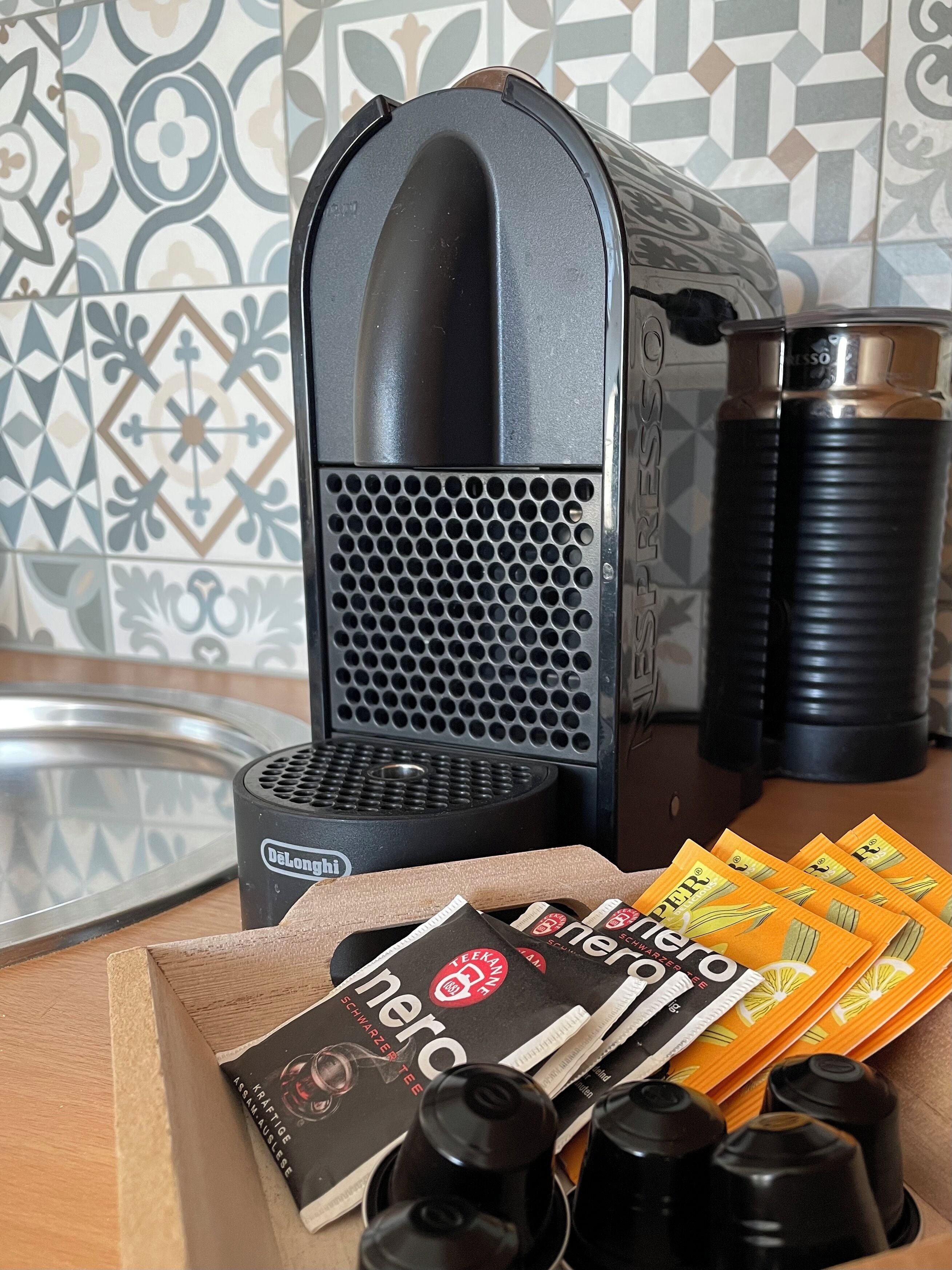 Una cafetera, un hervidor y cápsulas de café sobre una encimera de cocina.