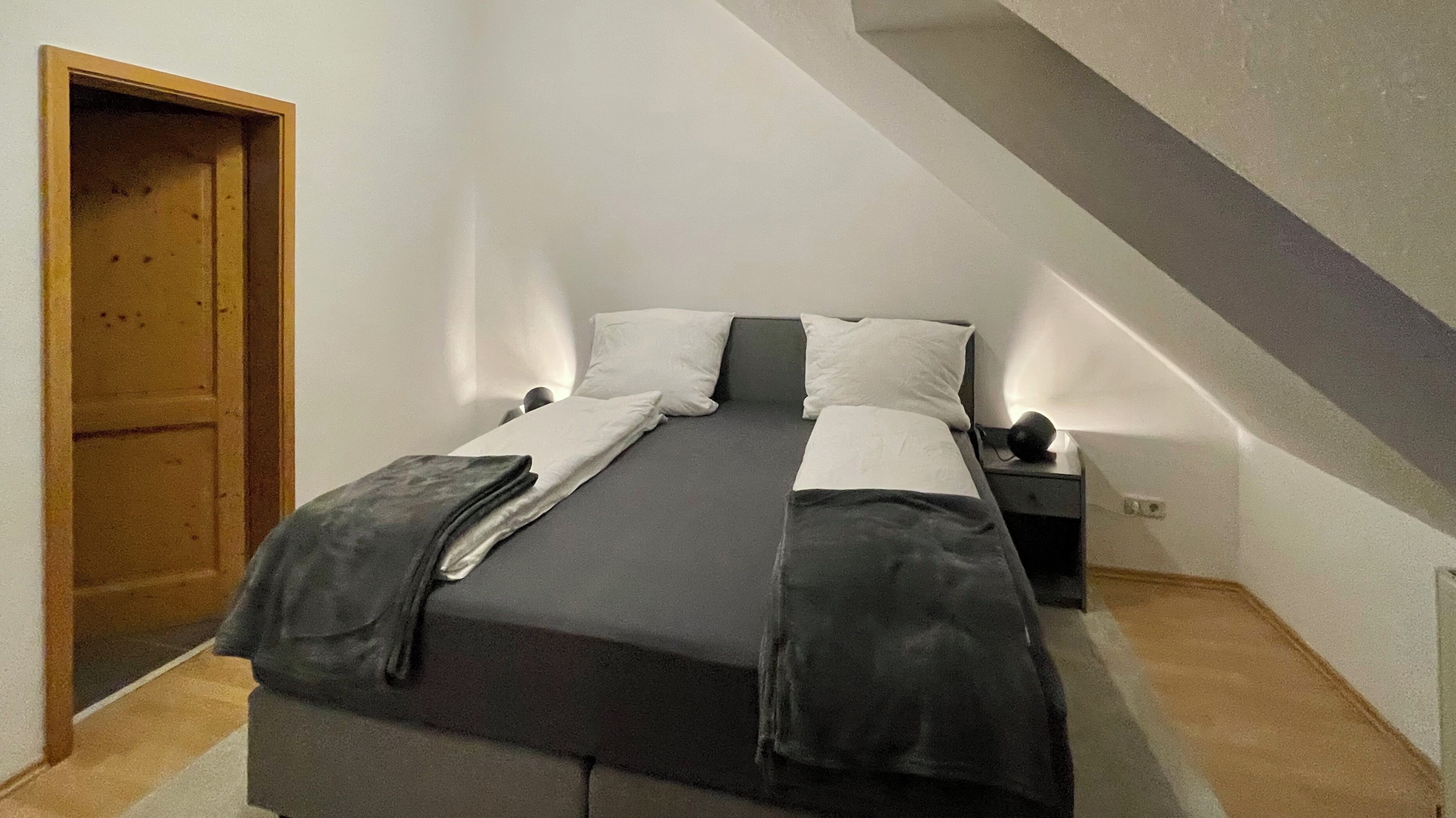 Een slaapkamer met een bed, nachtkastje, lamp en een deur.