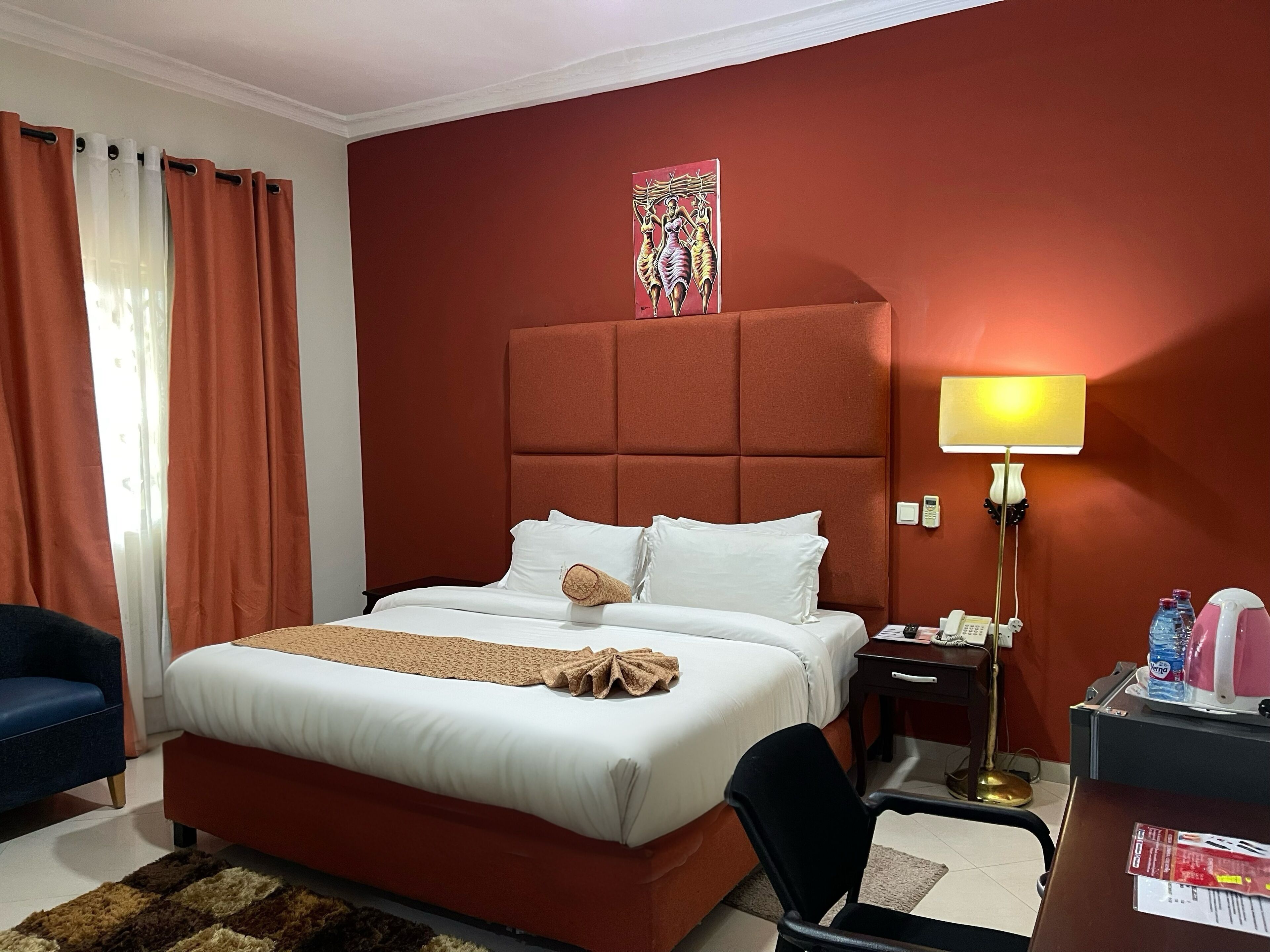 Una camera d'albergo con un letto grande, una scrivania con una lampada, una sedia e un quadro appeso al muro.