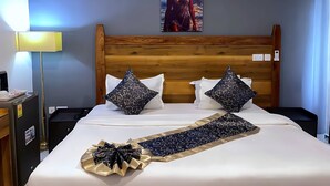 Habitació d'hotel amb un panell de fusta al capçal del llit, un quadre d'una persona a la vora del mar, una làmpada de nit i un llit ben fet amb coixins estampats i una funda decorativa per al capçal.