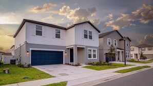A modern two-story residential building with a garage, well-maintained lawn, and a clear sky.