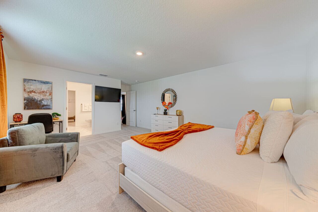 Une chambre à coucher avec un lit, un bureau, une chaise, une commode et un téléviseur fixé au mur.