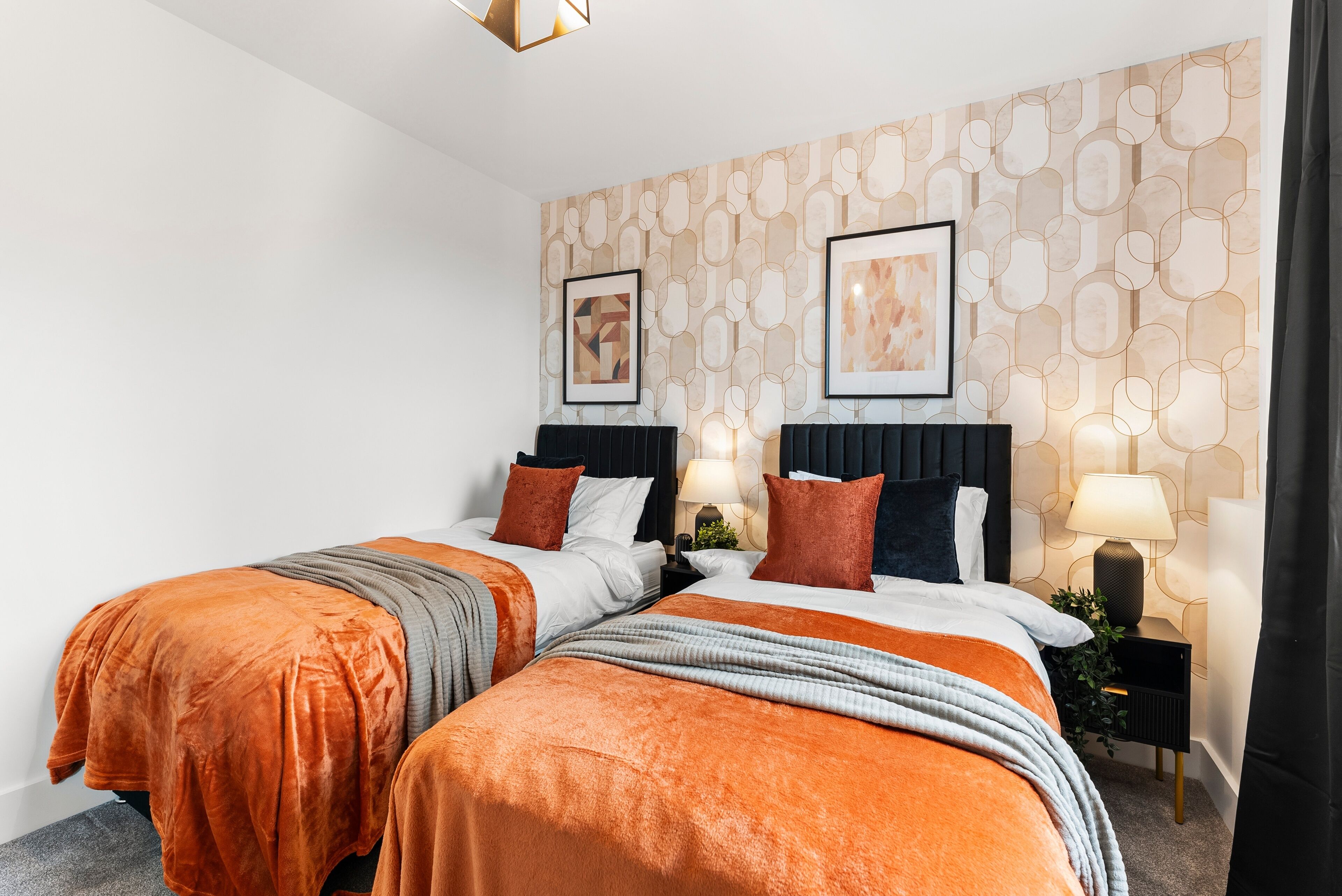 A double bed with orange and grey bedding, a nightstand with a lamp, and a wall with a geometric pattern.