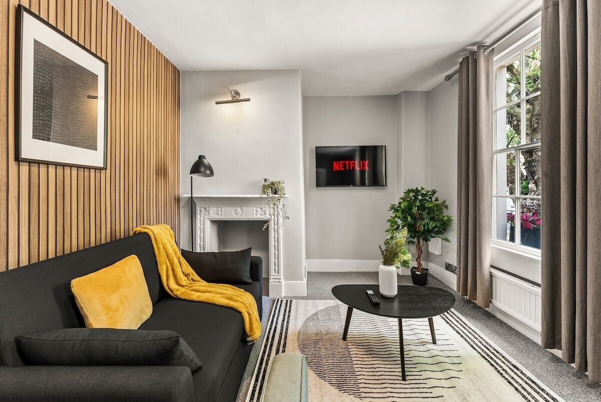 A modern living room with a black sofa, a fireplace, a TV, and a large window with curtains.